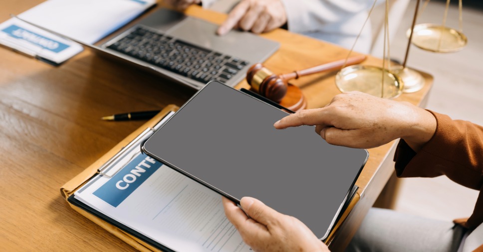 Mão usa tablet perto de martelo e balança para ilustrar a automação na controladoria jurídica.